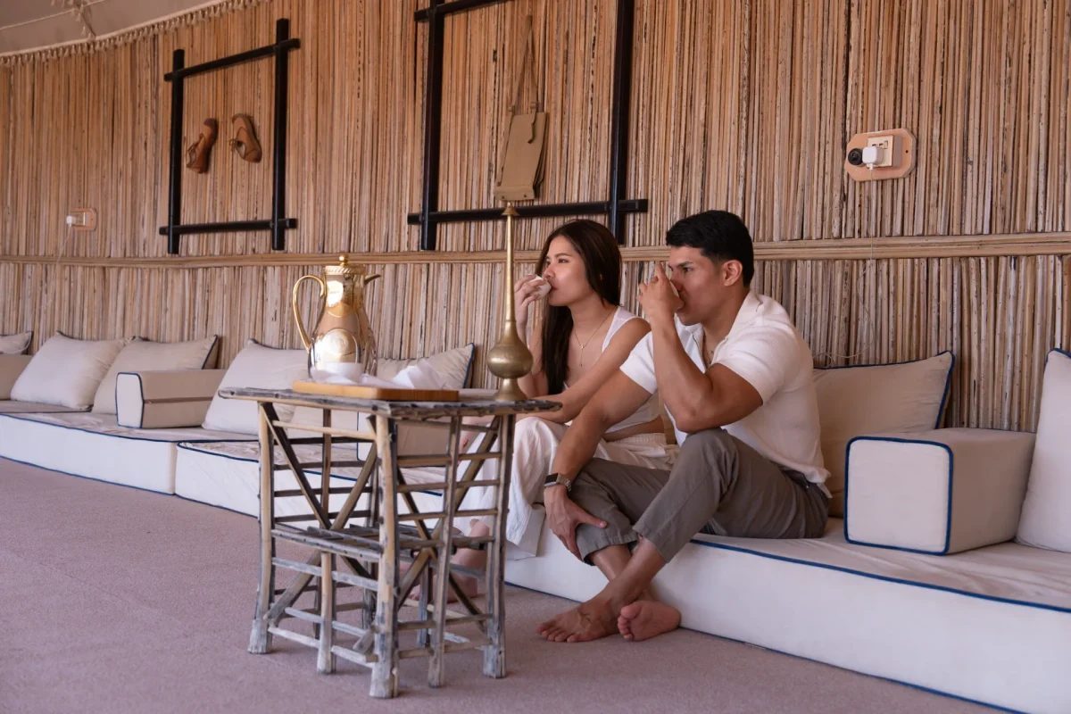 Guests drinking Arabic coffee beside a brass coffee pot at a Dubai desert camp