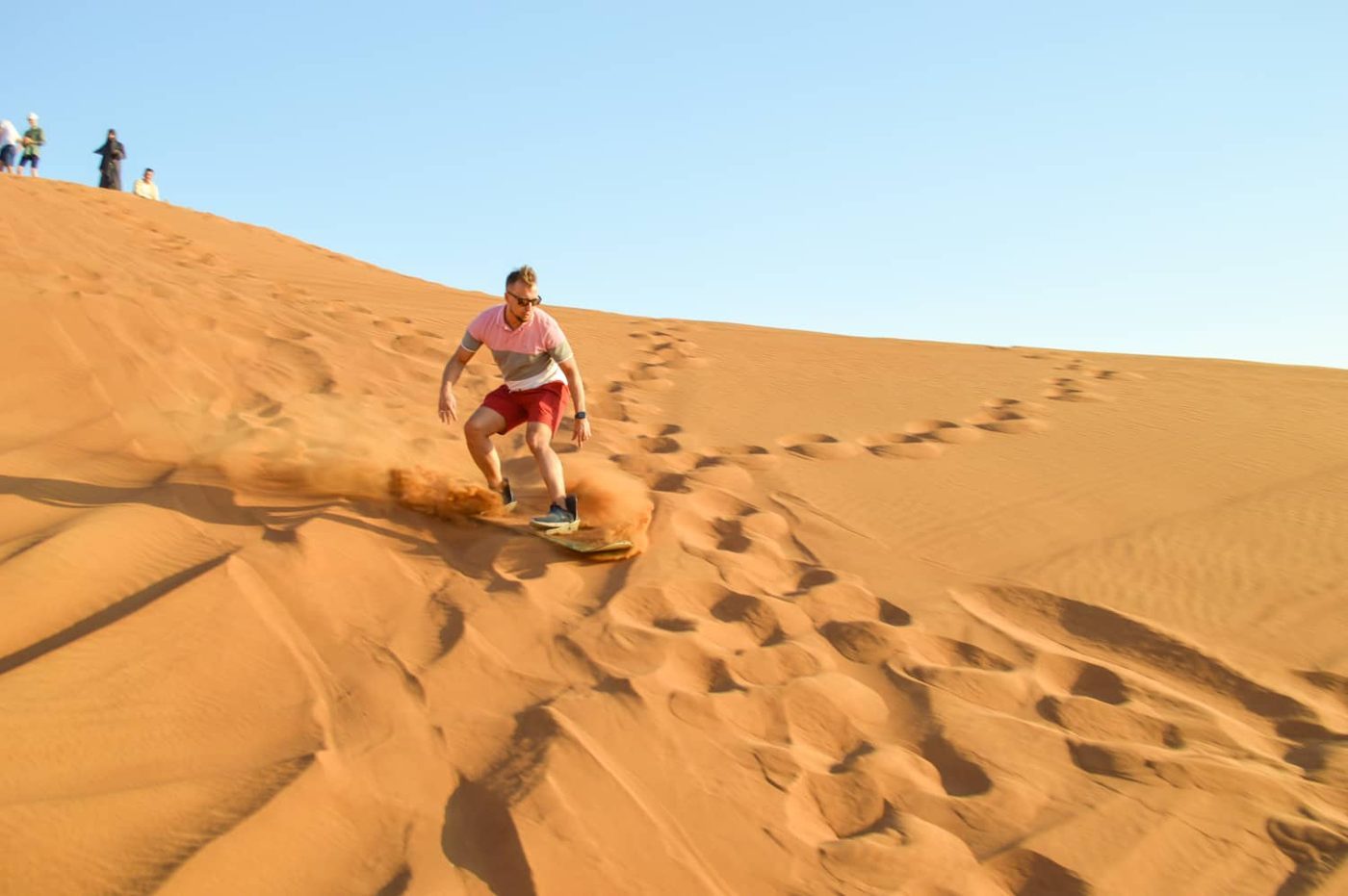 Man riding a sandboard down a sunlit desert dune