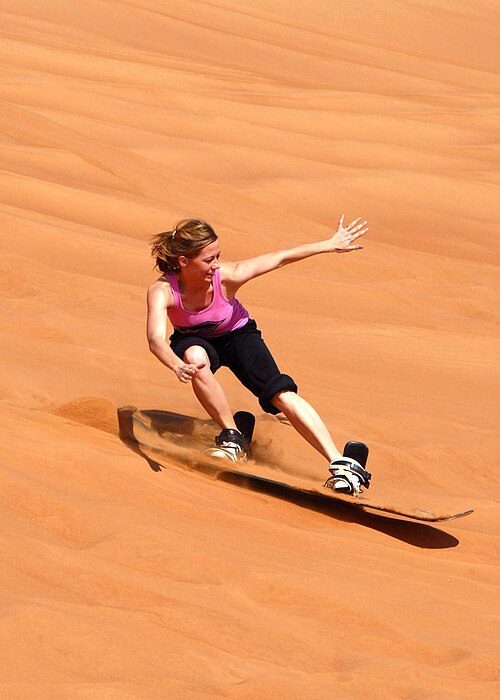 Woman sliding down an orange Dubai sand dune on a sandboard