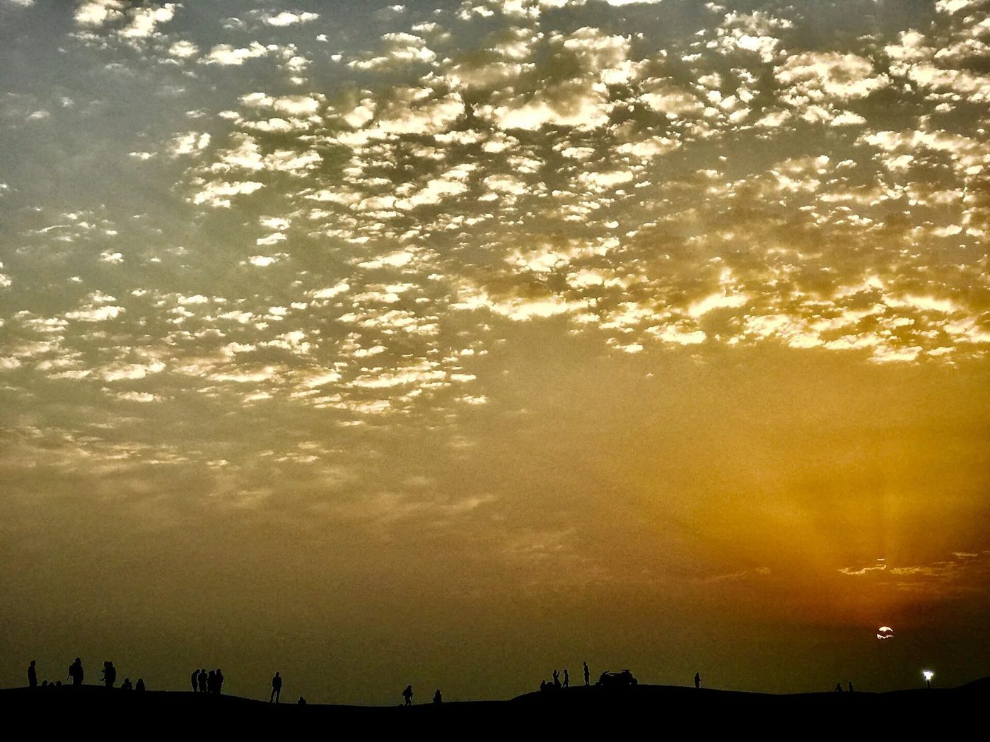 Early golden light shining through clouds above the desert horizon