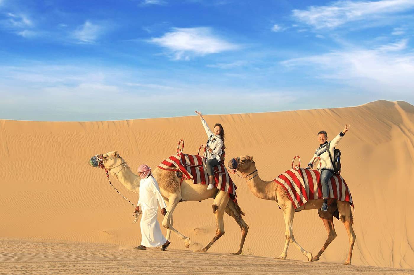 Visitors riding camels across the desert with a guide