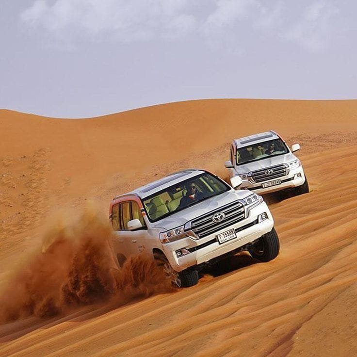 Two white four-wheel-drive vehicles driving over a sand dune