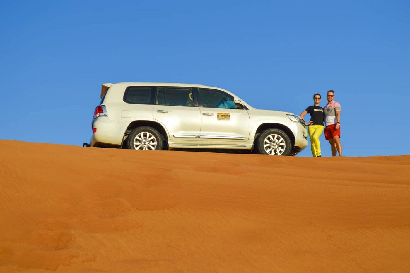 Guests beside a white four-wheel-drive vehicle on a Dubai sand dune