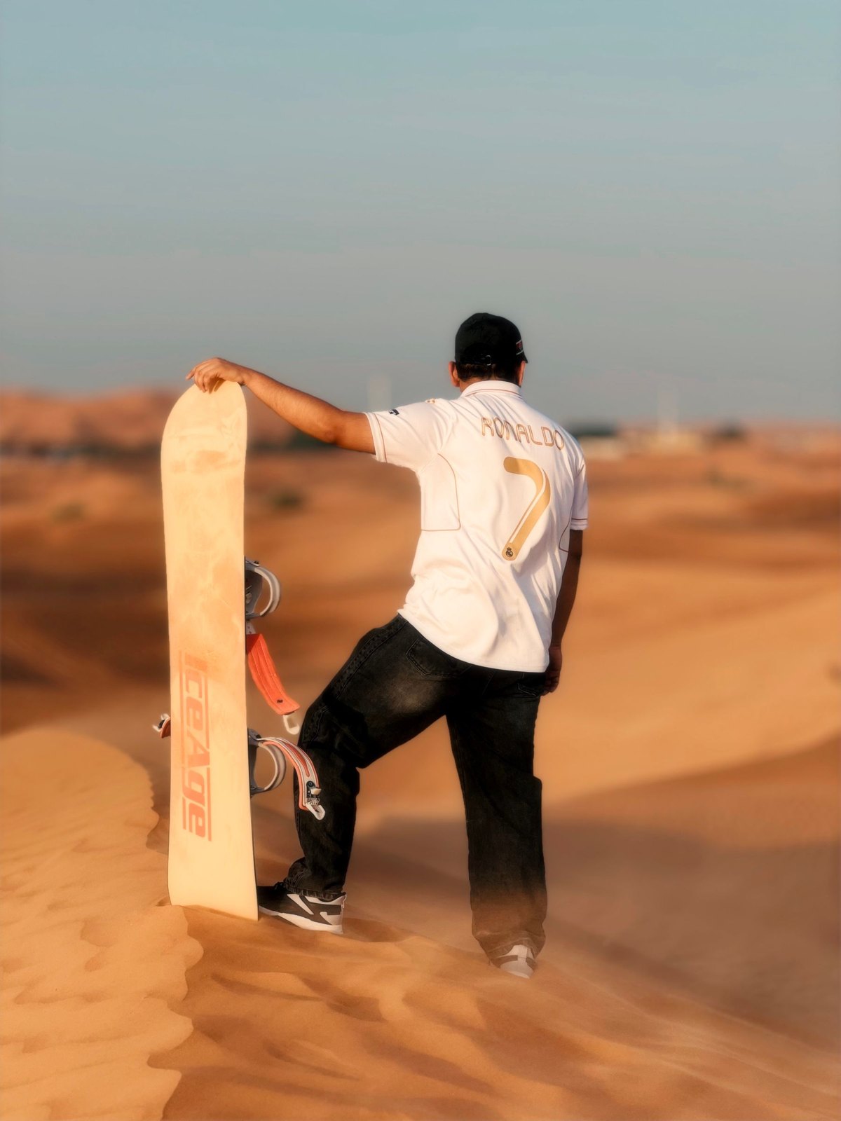 Man with a sandboard on a dune at sunset