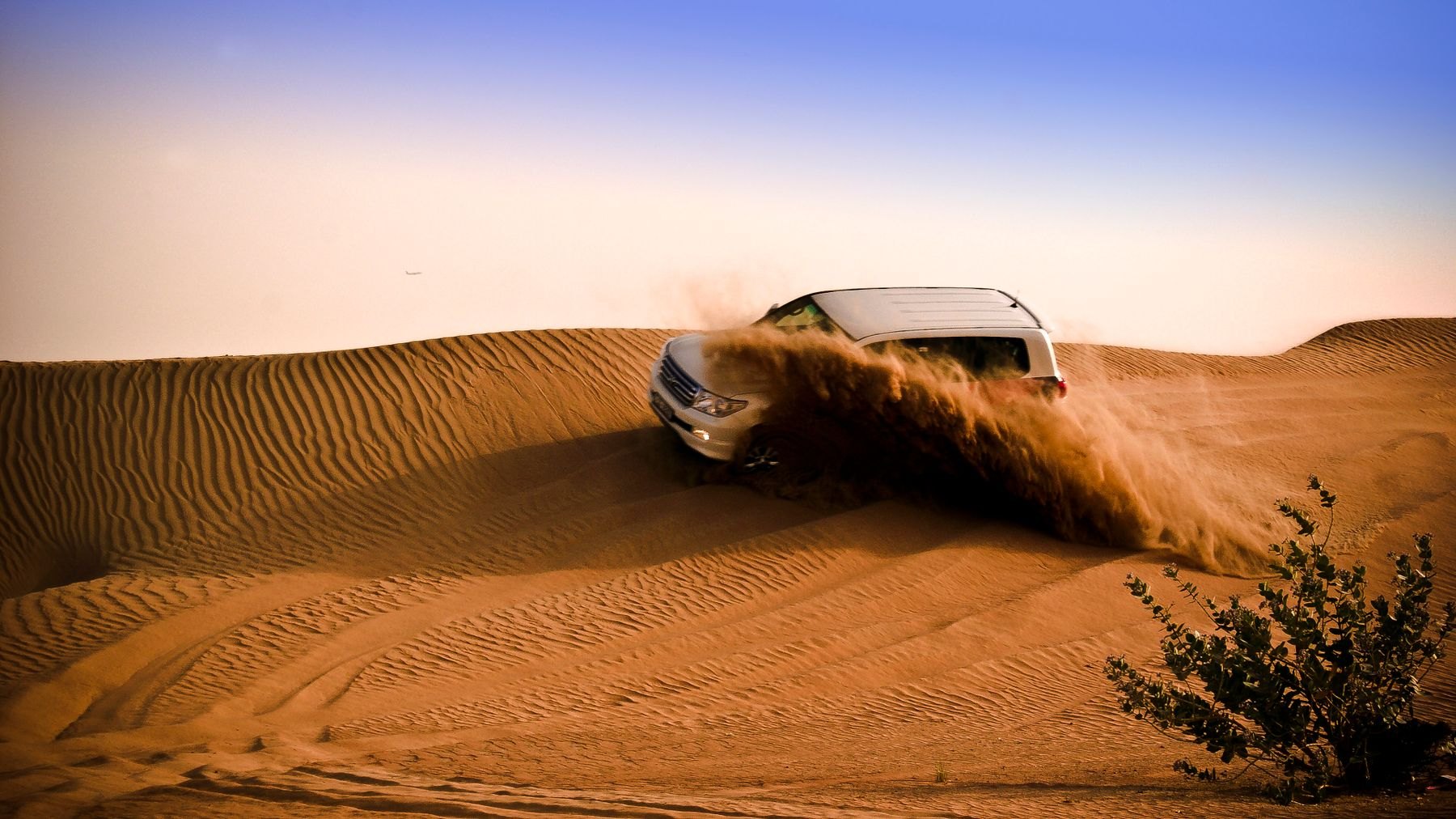 Four-wheel-drive vehicle kicking up sand on a dune